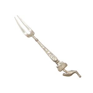 May include: A silver-toned metal serving fork featuring a two-pronged head and a decorative handle. The handle is adorned with an embossed leaf pattern and terminates in a detailed sculptural figure of a bird perched on a textured base.