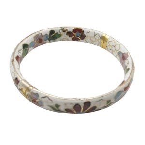 Könnte beinhalten: Weißes Emaille-Armreif-Armband mit einem Blumendesign in Rot, Blau, Grün und Gold. Das Armband hat einen goldfarbenen Verschluss. Die Blumen sind um das Armband angeordnet.