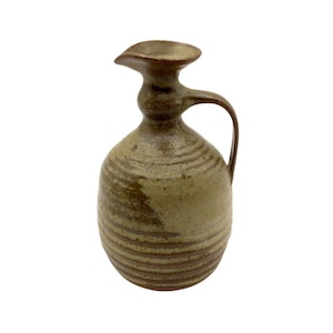 Puede incluir: Jarra de cerámica hecha a mano con pico y asa. La jarra tiene un cuerpo bulboso con rayas horizontales marrones y una combinación de colores verde claro y marrón. El pico es acampanado y el asa es curva.