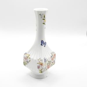 May include: A white porcelain vase with a floral and butterfly design. The vase has a narrow neck and a wide base with a fluted design.