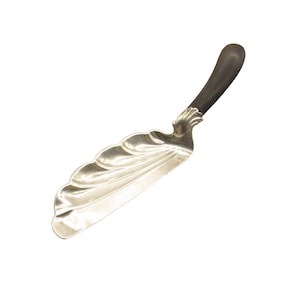 Könnte beinhalten: Silberfarbenes Servierutensil mit einem dunkelbraunen Griff. Das Utensil hat ein dekoratives, wellenförmiges Design auf der Servierfläche. Der Griff ist gebogen und scheint aus Holz oder einem ähnlichen Material zu bestehen. Zum Servieren von Speisen.