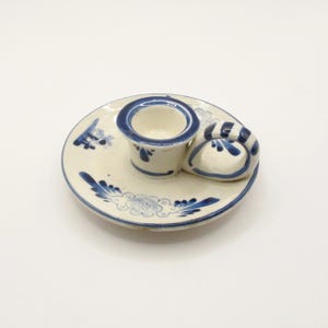 May include: A white ceramic candle holder with a blue and white floral design. The holder has a small, round base and a handle that is shaped like a heart.