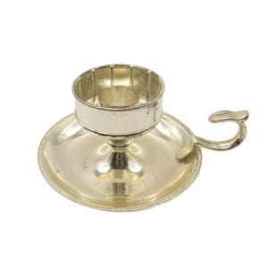 Può includere: Candeliere d'argento con base rotonda e manico. Il candeliere ha un design decorativo e una piccola coppa per una candela.