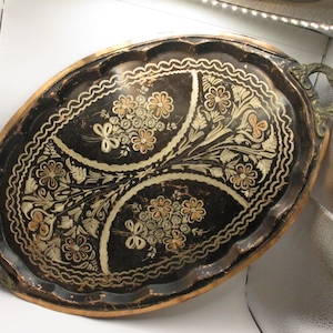 May include: Oval serving tray with a black background and floral design. The tray has a gold rim and handles, and the floral pattern includes white and orange accents. The tray is approximately 18 inches long.