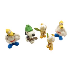 Könnte beinhalten: Eine Sammlung von Vintage-Cartoon-Charakterfiguren. Die Figuren umfassen einen gelbgesichtigen Hund mit weißem Körper und blauer Hose, einen weißen Hund mit grünem Hut und drei kleine Figuren mit gelben Haaren und grünen Schlägern.