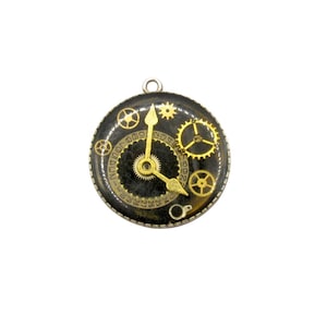 Puede incluir: Colgante redondo negro con engranajes y manecillas de reloj doradas. El colgante tiene un pequeño lazo en la parte superior para colgarlo. La esfera del reloj muestra una fecha y la palabra "LONDON".