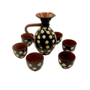 May include: A black ceramic pitcher and matching cups set. The pitcher has a brown handle and spout, and the set features a white polka dot pattern. The cups and pitcher have a brown interior.