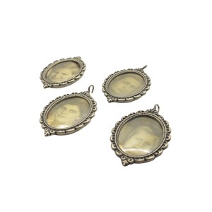 May include: Four antique silver-toned oval pendants, each with a small black and white portrait inside. The pendants have ornate, scalloped edges and a small loop at the top for hanging. The portraits appear to be of different people.