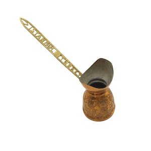 May include: A copper-colored Turkish coffee pot with a long handle. The handle is gold-colored and has the words "ISTANBUL TURKEY" etched into it. The pot has a decorative floral pattern around the base.