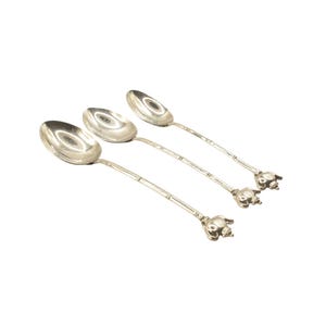 May include: Three silver spoons with bamboo-style handles and elephant head detailing. The spoons are arranged diagonally against a white backdrop, highlighting their polished, reflective surfaces. Each spoon is approximately 18 cm long.