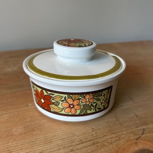 May include: White ceramic butter dish with a lid. The dish has a floral design with orange, red, and yellow flowers on a brown background. The lid has a matching floral pattern and a small handle.