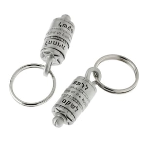 May include: Two silver-colored keychains with cylindrical pendants. Each pendant has engraved text and a star-shaped design. The keychains are on a white background.