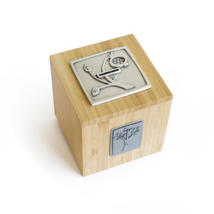 May include: A wooden box with a silver metal design of a tree with a pomegranate on top. The box has a slot for coins and is a decorative money box.