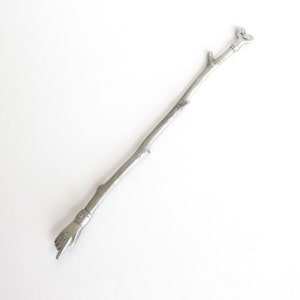 May include: A silver metal stirring stick with a hand and a heart design at each end.