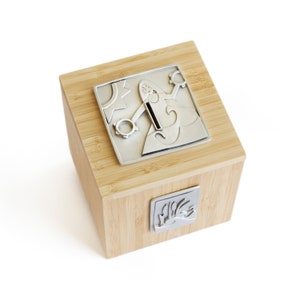 May include: A wooden box with a silver metal lid featuring a whimsical design. The lid has a slot for coins, making it a unique piggy bank.