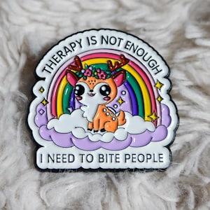 Peut inclure: Épinglette colorée en émail représentant un cerf de dessin animé avec une couronne de fleurs, sur fond d'arc-en-ciel et de nuages. L'épingle porte les inscriptions "THERAPY IS NOT ENOUGH" et "I NEED TO BITE PEOPLE".
