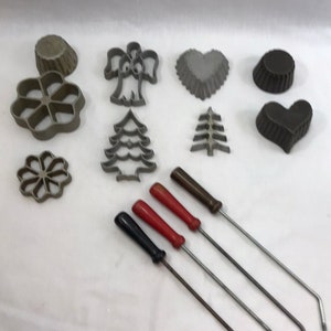 May include: A set of 10 vintage metal cookie cutters in various shapes, including a heart, angel, tree, and flower, along with four long metal handles with red and black handles.