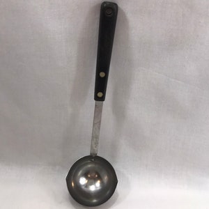 May include: A silver ladle with a black handle and two white buttons. The ladle has a rounded bowl and a long, thin handle.