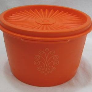 Puede incluir: Contenedor de almacenamiento de plástico naranja con tapa. La tapa tiene un diseño de sol y el contenedor tiene un diseño floral blanco.