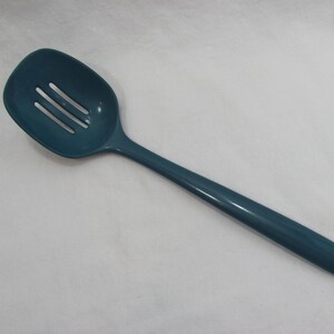 May include: A teal-colored slotted spoon with a long handle. The spoon's head is rectangular with three slots. The handle is smooth and tapers to a point. The kitchen utensil is made of plastic.