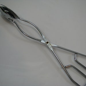 May include: Silver salad tongs with a spoon-shaped end for serving salad. The tongs are open and ready to use.