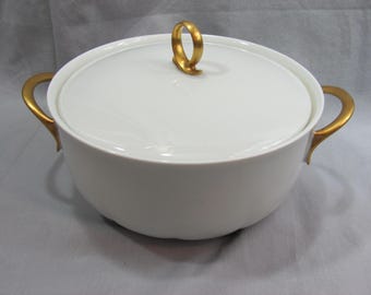 May include: White porcelain serving bowl with gold-colored handles and lid. The lid has a gold-colored ring handle.