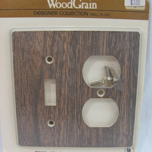 Puede incluir: Una placa de pared de madera de grano marrón con un interruptor de 2 gangues y una toma de corriente combinada. La placa está etiquetada como "Wood Grain Designer Collection Wall Plate" y "PWG4290 2-Gang Switch" y "PWG429C Combination".