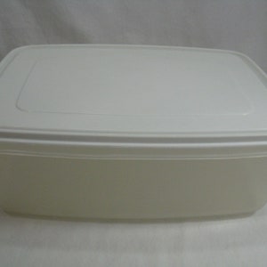 Puede incluir: Un recipiente rectangular de plástico blanco roto para guardar alimentos con tapa a juego. El recipiente tiene esquinas redondeadas y un aspecto ligeramente translúcido. La tapa encaja perfectamente.