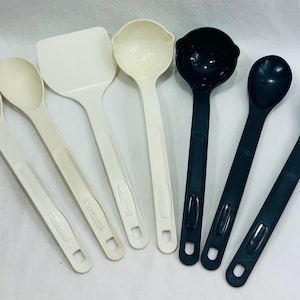 May include: A collection of seven kitchen utensils, including slotted spoons, a spatula, a ladle, and solid spoons. The utensils are in shades of white and dark teal. The handles have a hole for hanging.