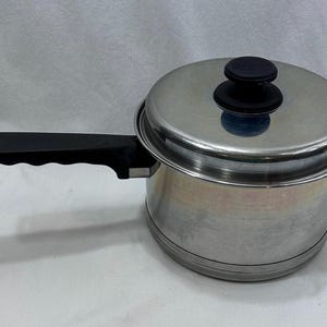 May include: A stainless steel saucepan with a lid and a black handle. The pot has a shiny, metallic finish and a black knob on the lid. The handle is ergonomically designed. A kitchen essential for cooking.