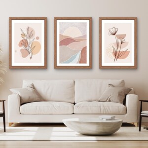 May include: Three framed wall art prints featuring a light color palette of beige, terracotta, and soft blue. The left print shows a botanical line drawing, the center depicts a landscape with a sun, and the right displays a floral line drawing.