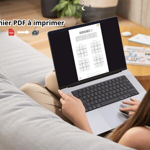 May include: A silver laptop displaying a Sudoku puzzle document on its screen. The screen shows the title Sudoku and four grid puzzles. Text on the image reads Fichier PDF &agrave; imprimer with a red PDF icon and a printer icon with an arrow.