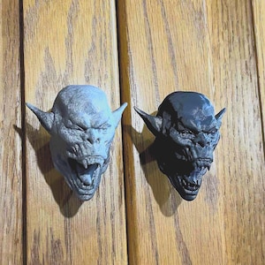 May include: Two decorative door knobs shaped like a goblin's head. One is gray and the other is black.