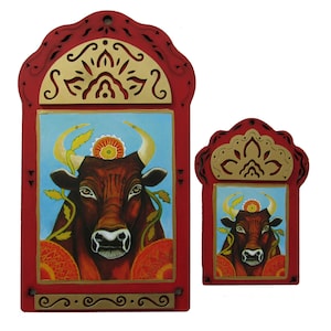 May include: Two red wooden frames with gold accents and intricate designs. Each frame features a painted image of a brown bull with a floral crown and a blue background.