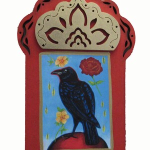 May include: A red wooden frame with a gold decorative top and a blue background. The frame contains a painting of a black crow perched on a red sphere with yellow and red flowers.