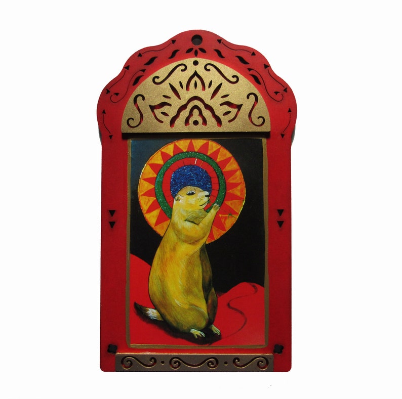 May include: A red wooden frame with a gold-painted design surrounds a painting of a prairie dog wearing a blue and green hat. The prairie dog is standing on a red platform with a yellow sun behind it.