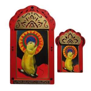May include: Two red wooden frames with gold accents and intricate designs. The frames contain paintings of a prairie dog with a colorful halo. The larger frame is taller than the smaller frame.