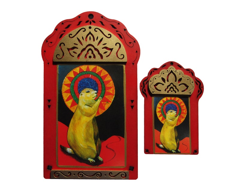 May include: Two red wooden frames with gold accents and intricate designs. The frames contain paintings of a prairie dog with a colorful halo. The larger frame is taller than the smaller frame.