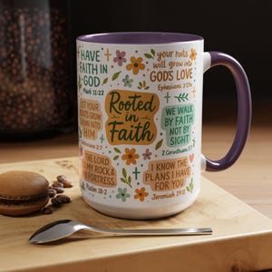 May include: A white ceramic mug with a purple handle and rim, decorated with the words "Rooted in Faith" and Bible verses, alongside floral illustrations. The mug sits on a wooden board with a spoon and a macaron.