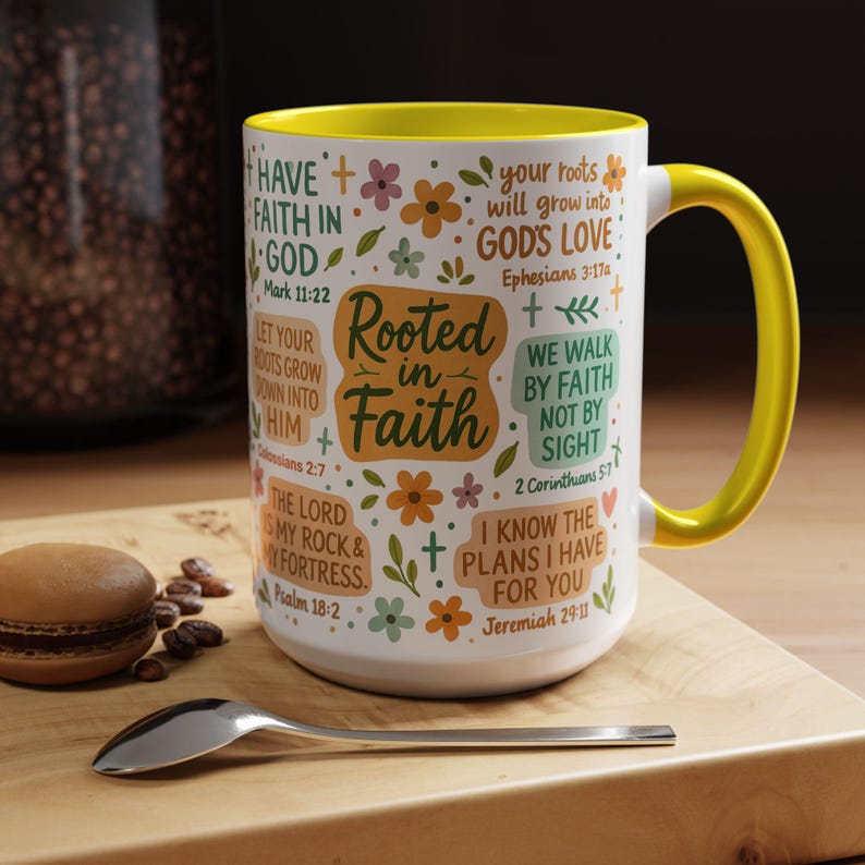 May include: White ceramic mug with a yellow interior and handle. The mug is decorated with floral designs and inspirational text, including "Rooted in Faith" and Bible verses. A spoon and a pastry are on a wooden surface.