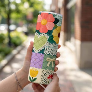 Può includere: Un bicchiere a tema floreale con un design patchwork con fiori, cuori e pizzo. Il bicchiere ha un corpo in acciaio inossidabile e un motivo colorato e stravagante. Il design include un fungo rosso, un tulipano giallo e un motivo a quadretti verdi.