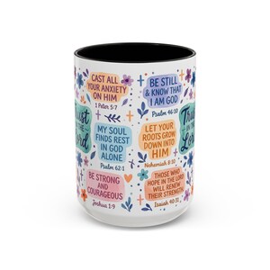 May include: White ceramic mug with a black interior, decorated with colourful floral and leaf designs. The mug features inspirational quotes and Bible verses in various fonts and colours, including "Cast All Your Anxiety On Him" and "Be Still & Know That I Am God."