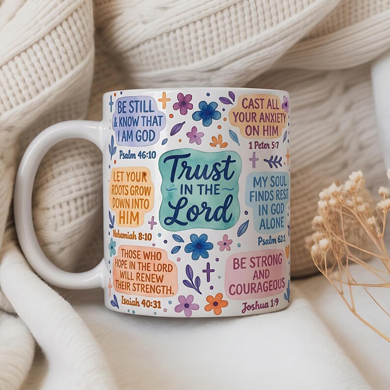 May include: White ceramic mug with a curved handle, decorated with floral accents and inspirational text. The mug features the words "Trust in the Lord" and various Bible verses in a colorful design. The mug is set against a soft, textured background.