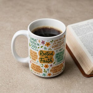 May include: White ceramic coffee mug filled with dark coffee, featuring the words "Rooted in Faith" and various Bible verses in a colorful floral design. A book is open in the background.
