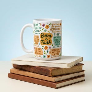 May include: White ceramic mug with the words "Rooted in Faith" and Bible verses. The mug has colourful floral and cross designs. The mug is on a stack of books. The books are in a variety of colours.