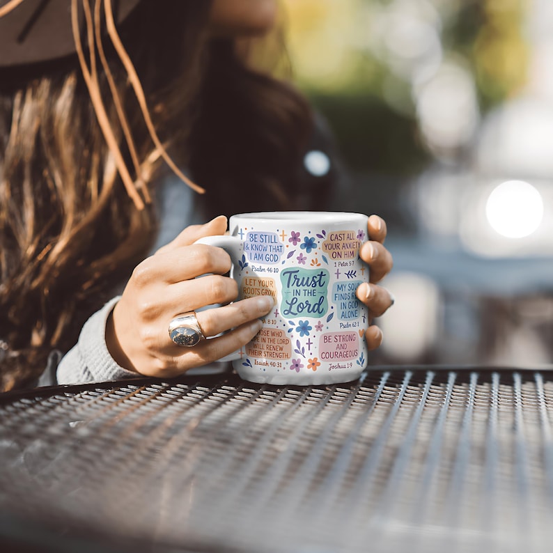May include: White ceramic mug with the text "Trust in the Lord" in a teal box, surrounded by floral and script designs. The mug also features various Bible verses in a mix of colours.