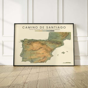 May include: A framed wall art print featuring a topographic map of the Iberian Peninsula titled CAMINO DE SANTIAGO. The map displays 9 routes, a total distance of 4400 km, and the finish point of Santiago de Compostela in black text on cream.