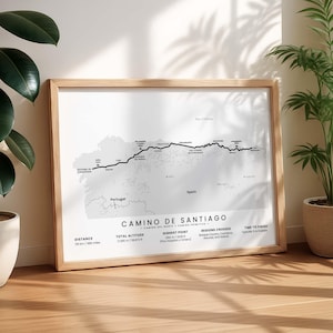 May include: A framed map print titled Camino de Santiago, featuring a black line route across a light gray map of northern Spain. Text includes distance of 486 miles, total altitude of 58,972 ft, and highest point of 4,239 ft.