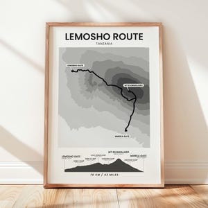 May include: A framed wall art print titled Lemosho Route Tanzania, featuring a grayscale topographic map of the mountain path with labelled gates and camps, and a bottom elevation profile showing 70 KM / 43 MILES of total distance.