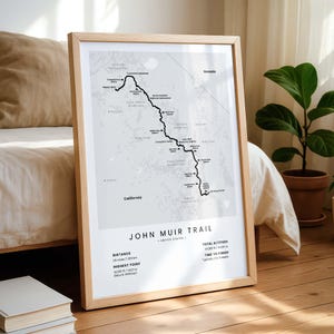 May include: A framed map print of the John Muir Trail in the United States, featuring a light gray topographic background with a black line indicating the trail route, marked locations, and text detailing distance, elevation, and completion time.